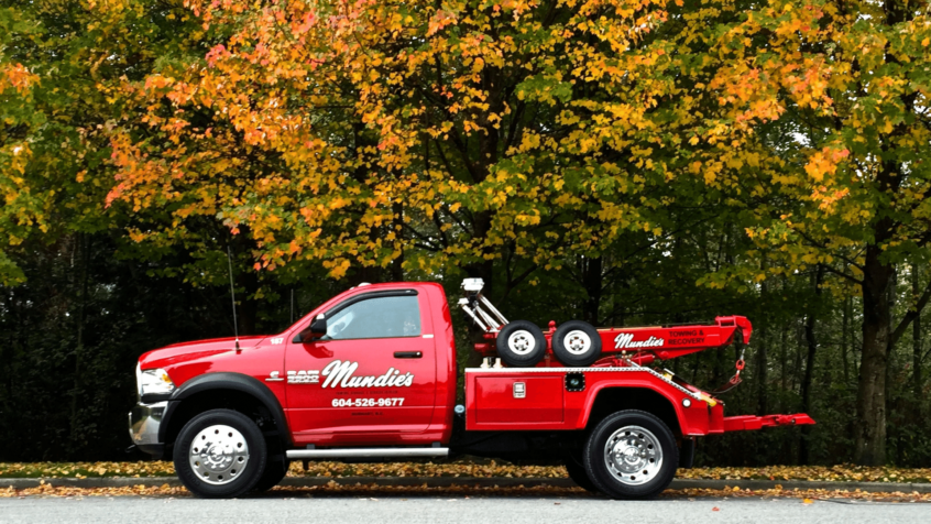 Image of Mundie's Towing and Recovery light-duty tow truck parked in front of trees.